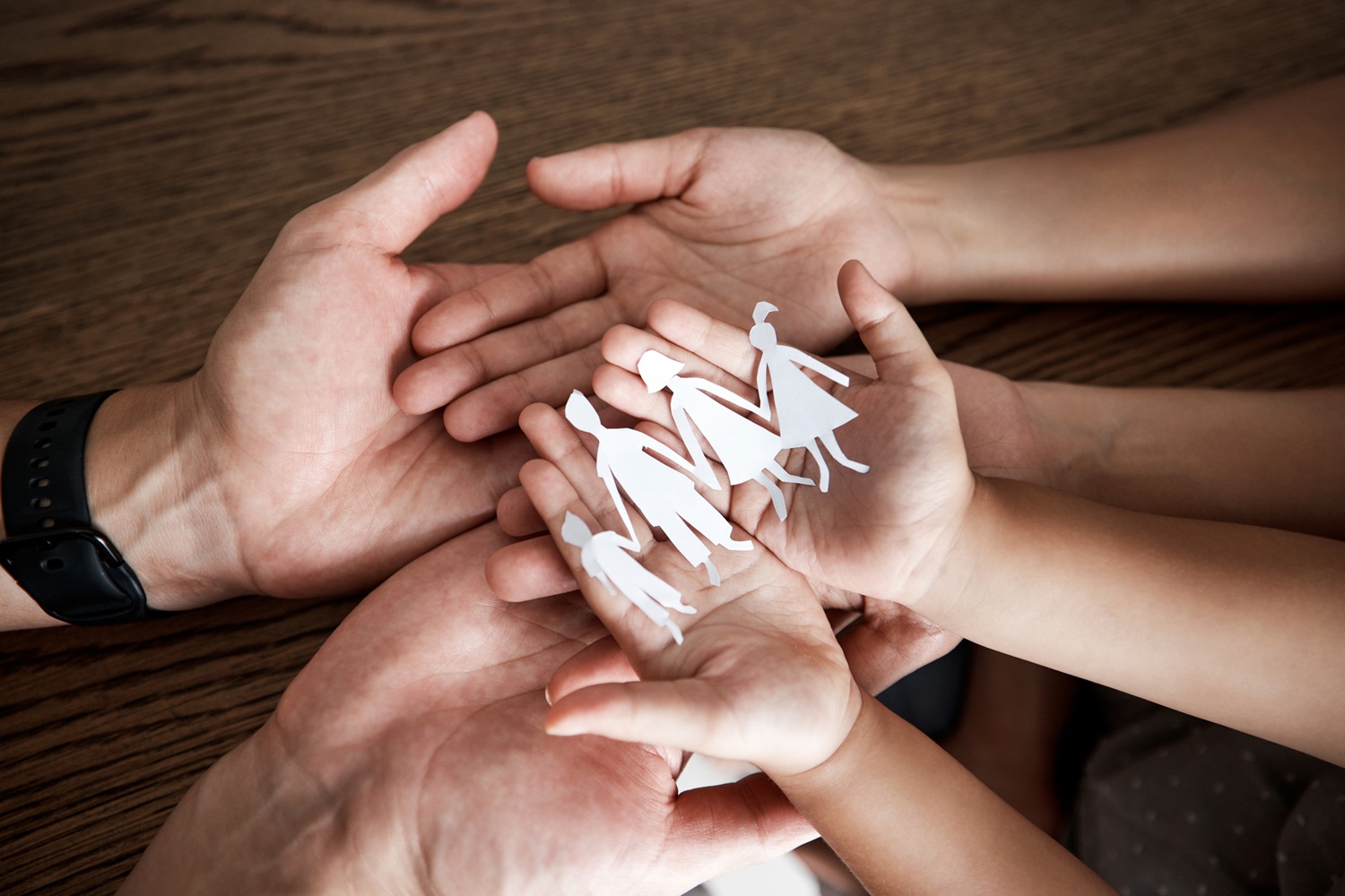 Hands, paper cutout family and house on table for sign, symbol or icon of support, love and solidarity. Art design with mother, father and children together for safety, trust and insurance in home.