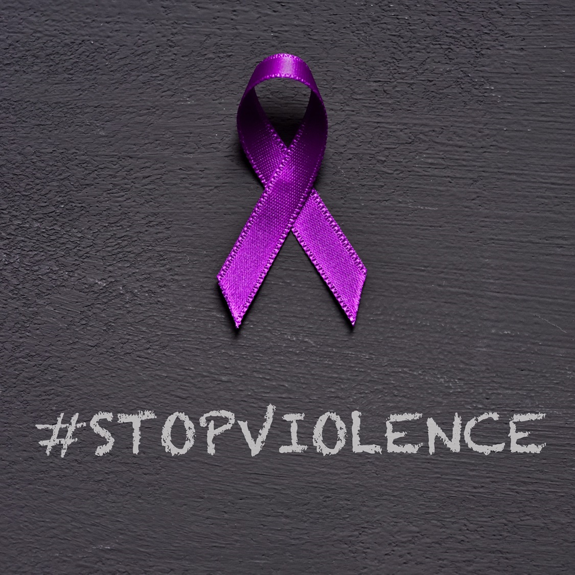 closeup of a purple ribbon, for the awareness about the unacceptability of the violence against women, and the text stop violence on a dark gray background